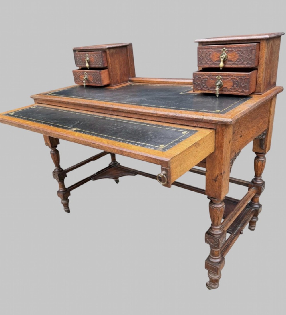 Victorian carved oak writing desk featuring a leather inset surface, two raised drawer cabinets on the top, two carved frieze drawers with brass drop handles, turned legs, and stretchers. View IV