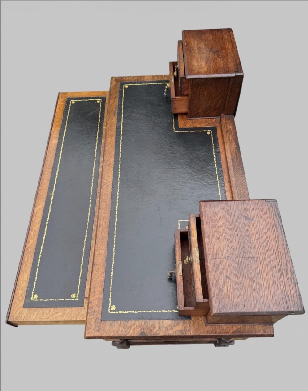 Victorian carved oak writing desk featuring a leather inset surface, two raised drawer cabinets on the top, two carved frieze drawers with brass drop handles, turned legs, and stretchers. View V