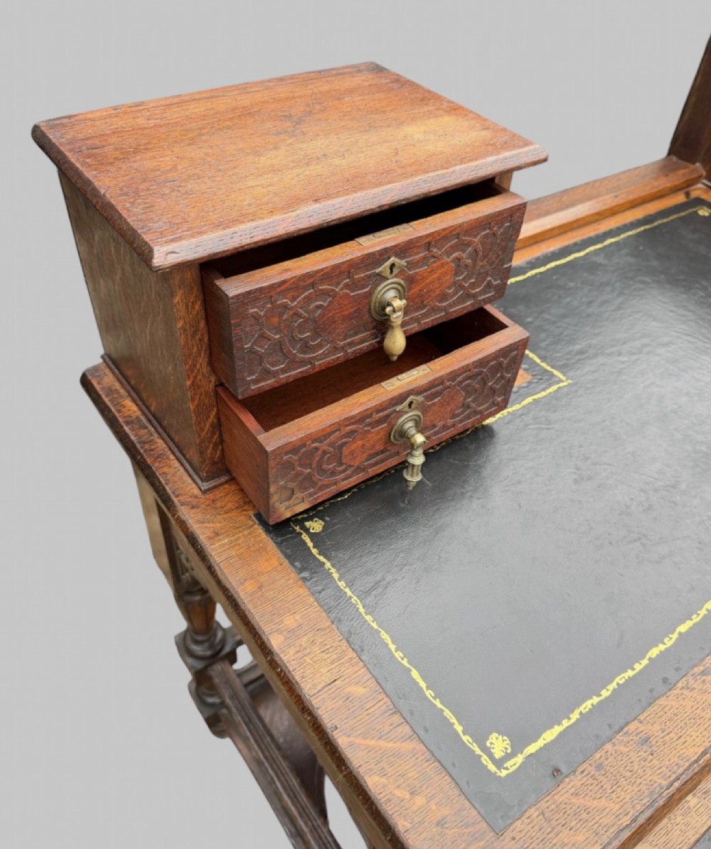 Victorian carved oak writing desk featuring a leather inset surface, two raised drawer cabinets on the top, two carved frieze drawers with brass drop handles, turned legs, and stretchers. View VII