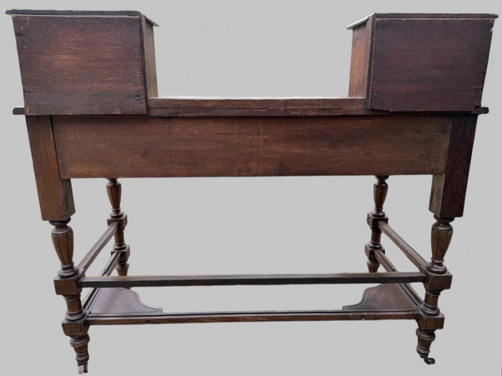 Victorian carved oak writing desk featuring a leather inset surface, two raised drawer cabinets on the top, two carved frieze drawers with brass drop handles, turned legs, and stretchers. View XI