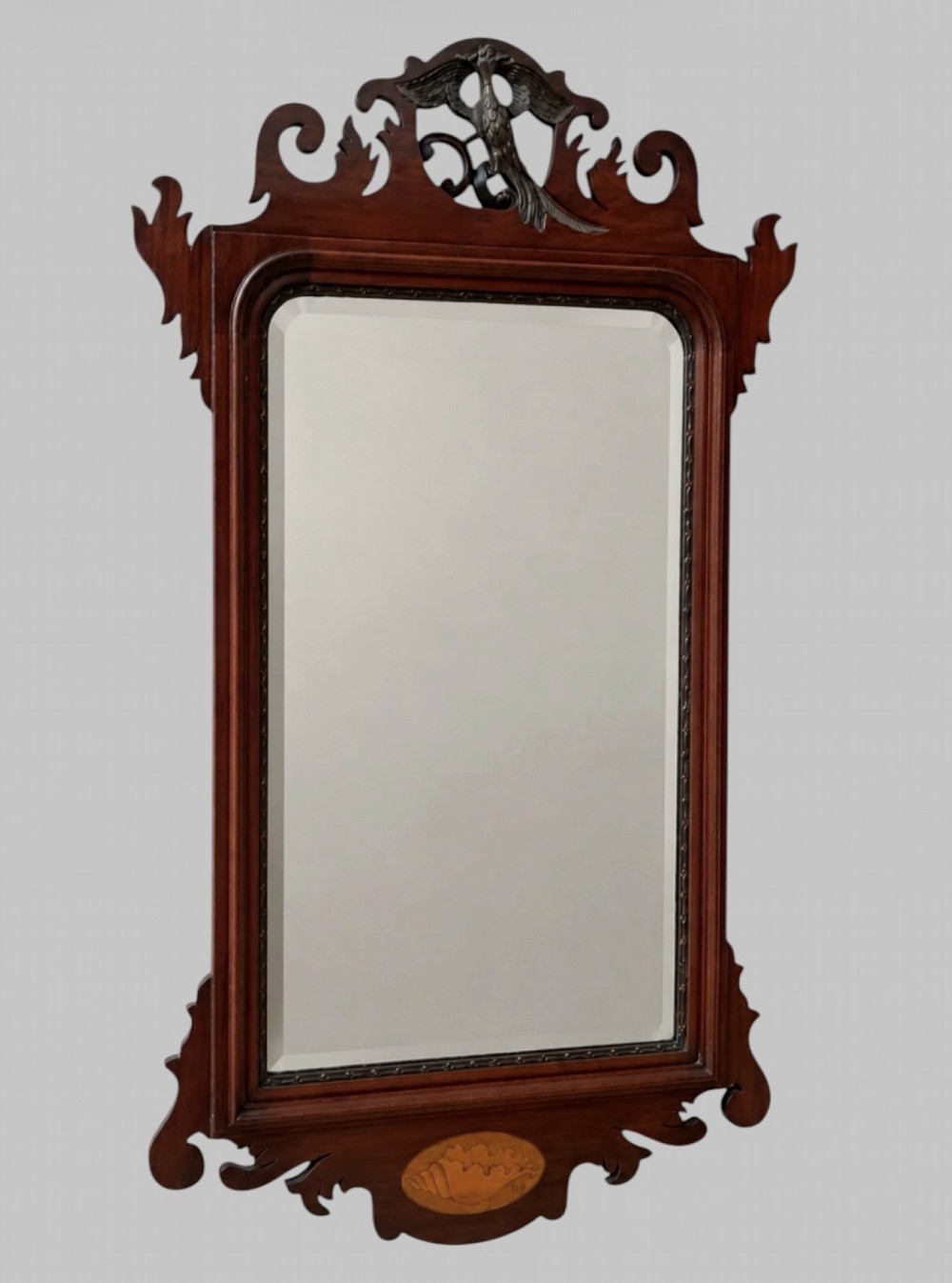 A tall Victorian Chippendale Revival mahogany wall mirror with a scrollwork fretcut frame, a crest depicting a bird, an oval shell inlay at the base, and bevelled glass.