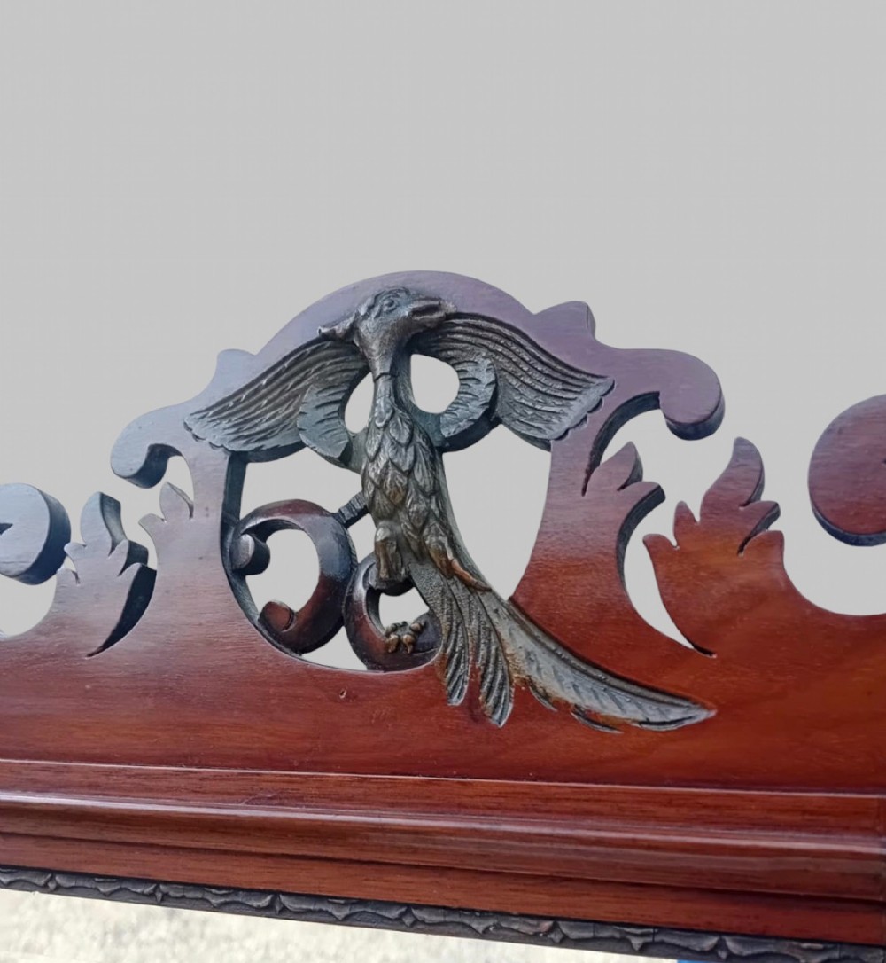 A tall Victorian Chippendale Revival mahogany wall mirror with a scrollwork fretcut frame, a crest depicting a bird, an oval shell inlay at the base, and bevelled glass. View IV