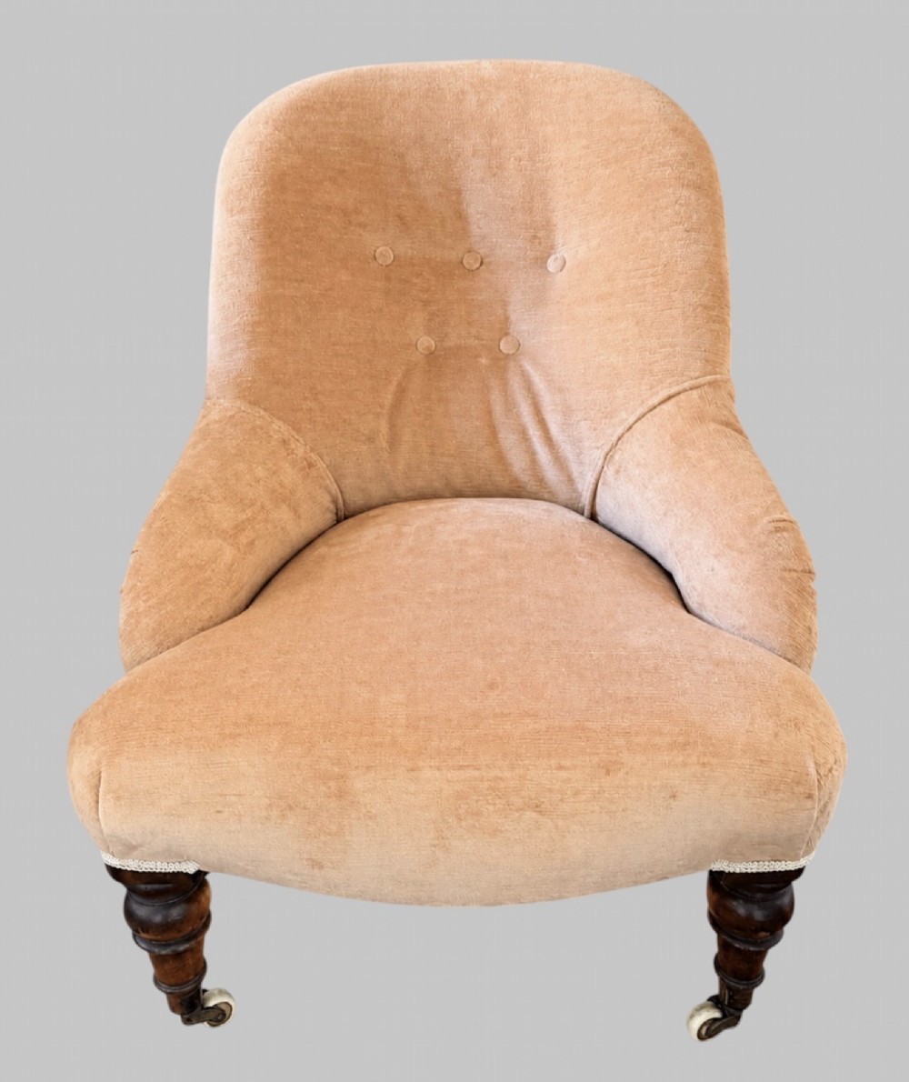 A profile view of a low Victorian iron-back nursing chair upholstered in beige velvet with printed pattern fabric sides and turned wooden legs on castors. View II