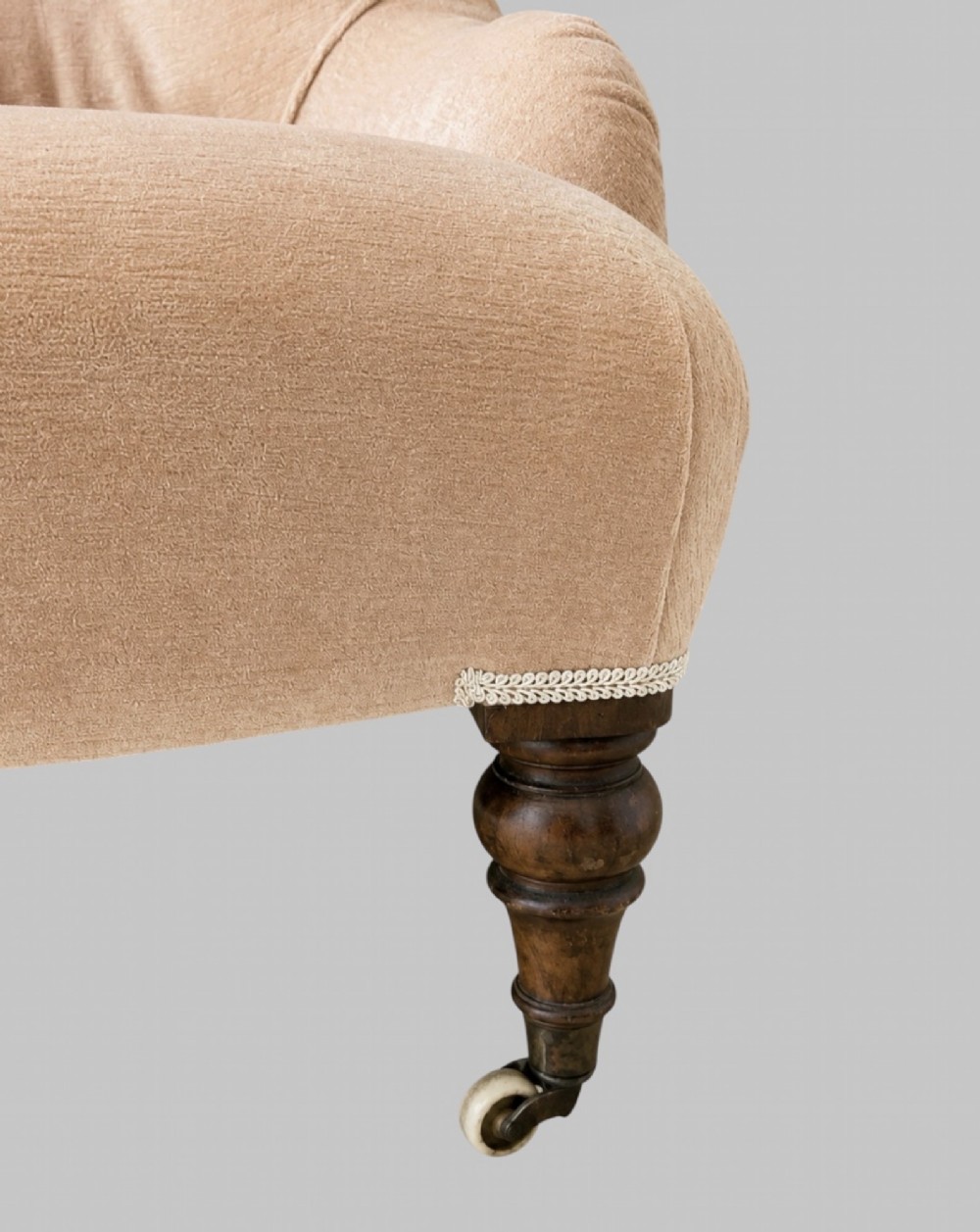 A profile view of a low Victorian iron-back nursing chair upholstered in beige velvet with printed pattern fabric sides and turned wooden legs on castors. View V