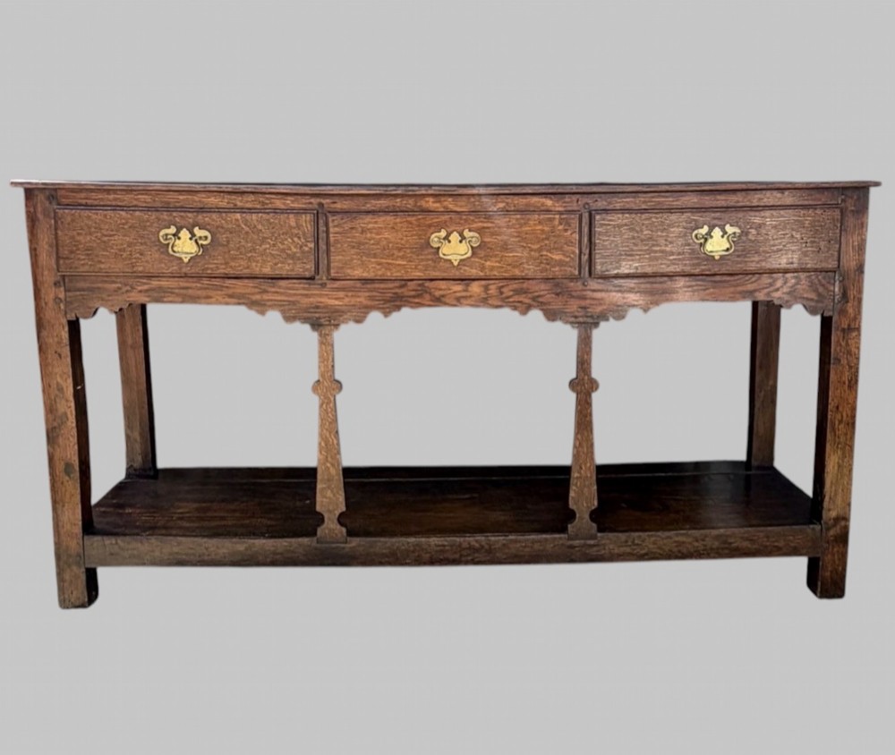 An 18th-century Welsh oak potboard dresser base featuring three frieze drawers with brass handles, a shaped apron, and a lower shelf.