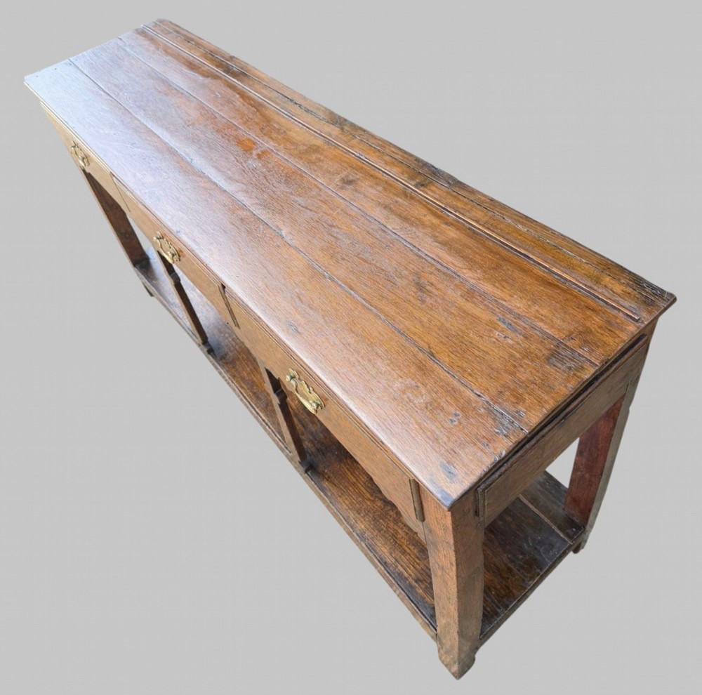 An 18th-century Welsh oak potboard dresser base featuring three frieze drawers with brass handles, a shaped apron, and a lower shelf. View III