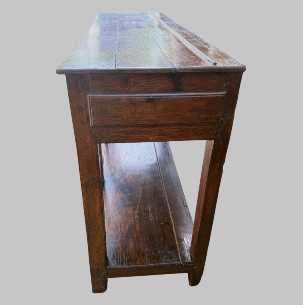 An 18th-century Welsh oak potboard dresser base featuring three frieze drawers with brass handles, a shaped apron, and a lower shelf. View IV