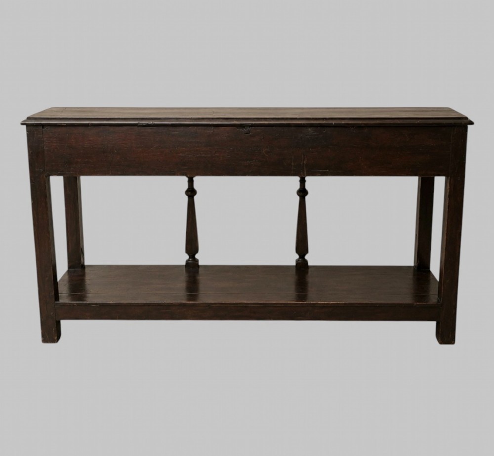 An 18th-century Welsh oak potboard dresser base featuring three frieze drawers with brass handles, a shaped apron, and a lower shelf. View V