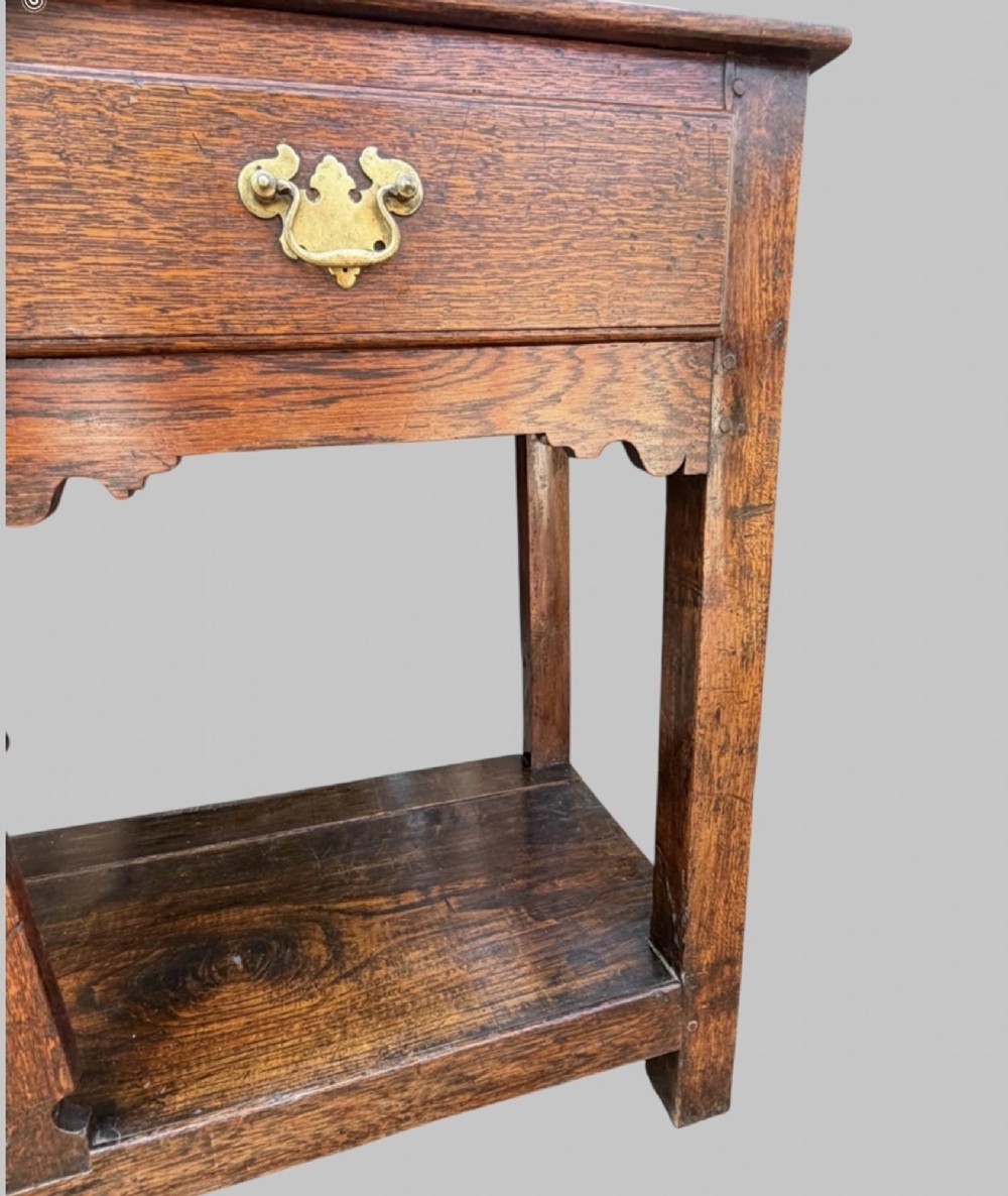An 18th-century Welsh oak potboard dresser base featuring three frieze drawers with brass handles, a shaped apron, and a lower shelf. View VI