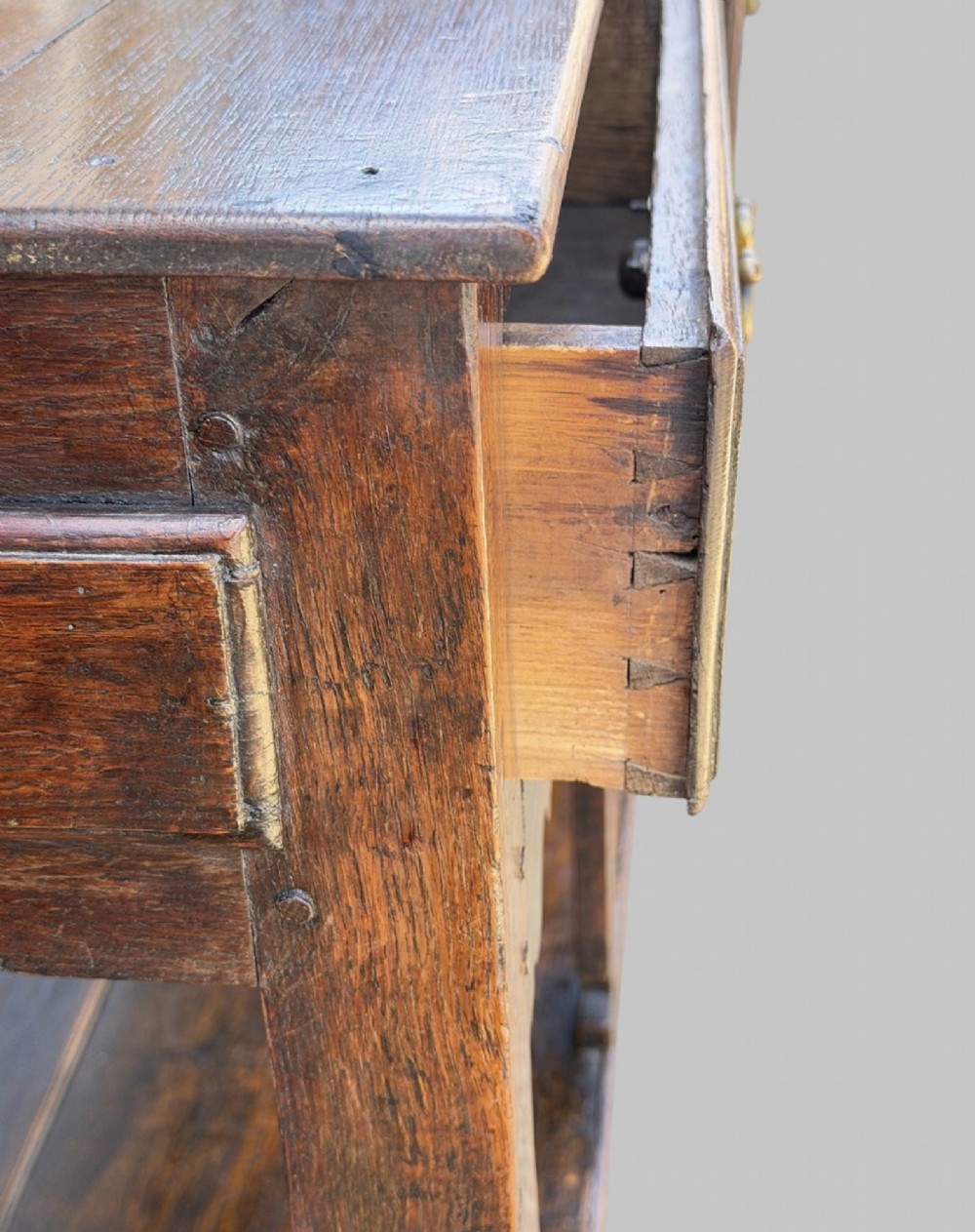 An 18th-century Welsh oak potboard dresser base featuring three frieze drawers with brass handles, a shaped apron, and a lower shelf. View VIII