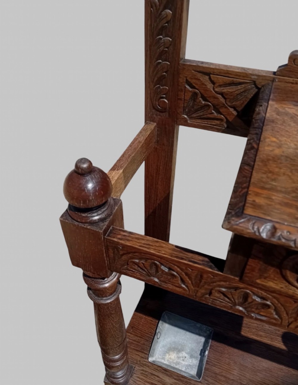 An antique carved dark oak hall stand featuring a central mirror, relief Green Man carved face motifs, hanging pegs, a middle drawer, and an umbrella rack base with metal drip trays. View VI