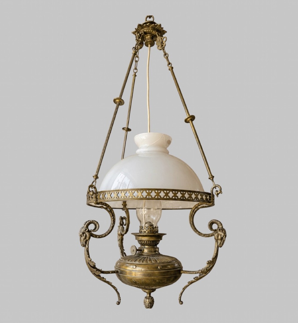A late Victorian brass hanging lamp featuring a white opaline glass shade, decorative rams head side scrolls, and a central burner unit.