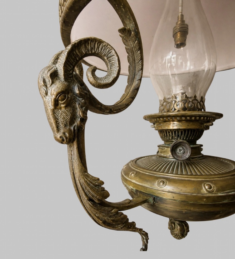 A late Victorian brass hanging lamp featuring a white opaline glass shade, decorative rams head side scrolls, and a central burner unit. View IV
