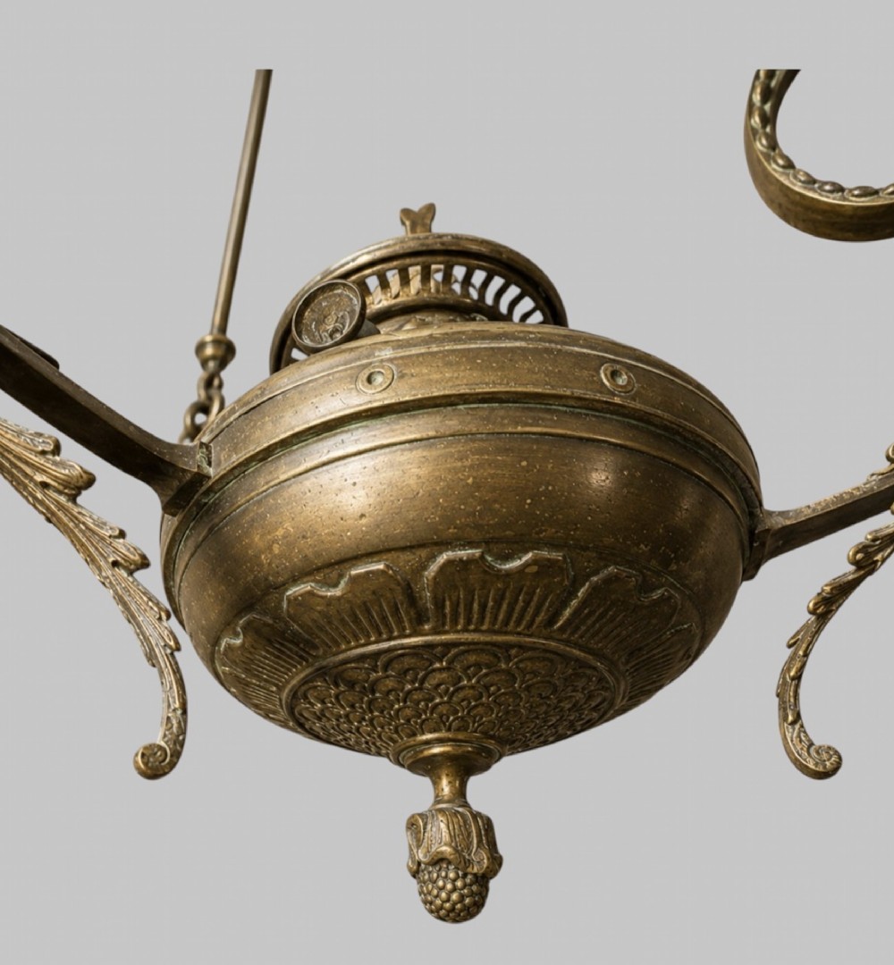 A late Victorian brass hanging lamp featuring a white opaline glass shade, decorative rams head side scrolls, and a central burner unit. View VI