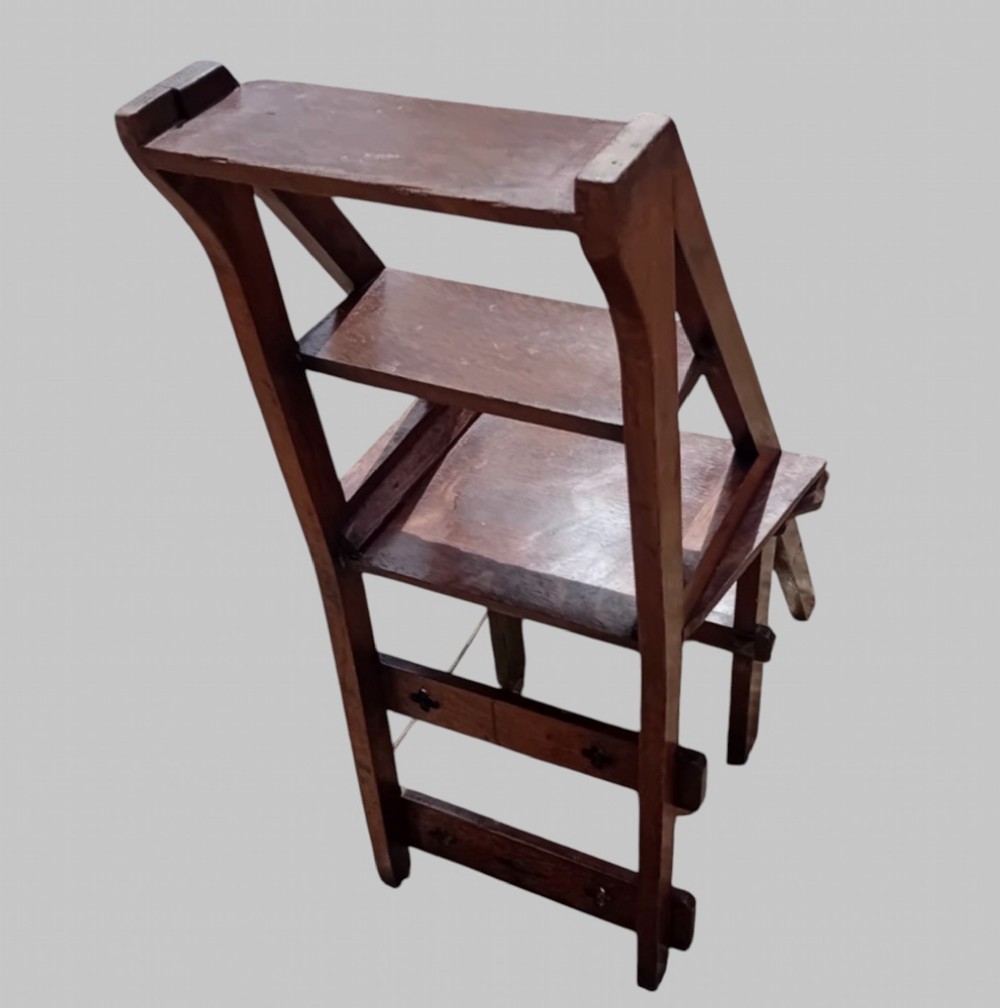 A late Victorian dark oak metamorphic chair featuring pierced trefoil cutouts on the backrest that hinges open to transform into a set of three library steps. View V