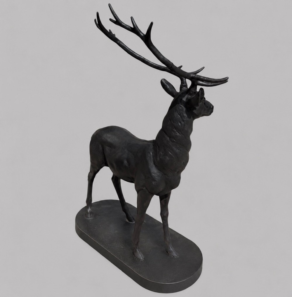 A patinated dark bronze sculpture depicting a standing young stag with antlers fixed onto an oval base. View III