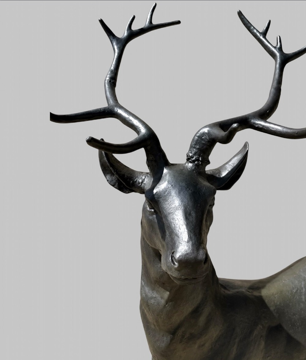 A patinated dark bronze sculpture depicting a standing young stag with antlers fixed onto an oval base. View IV
