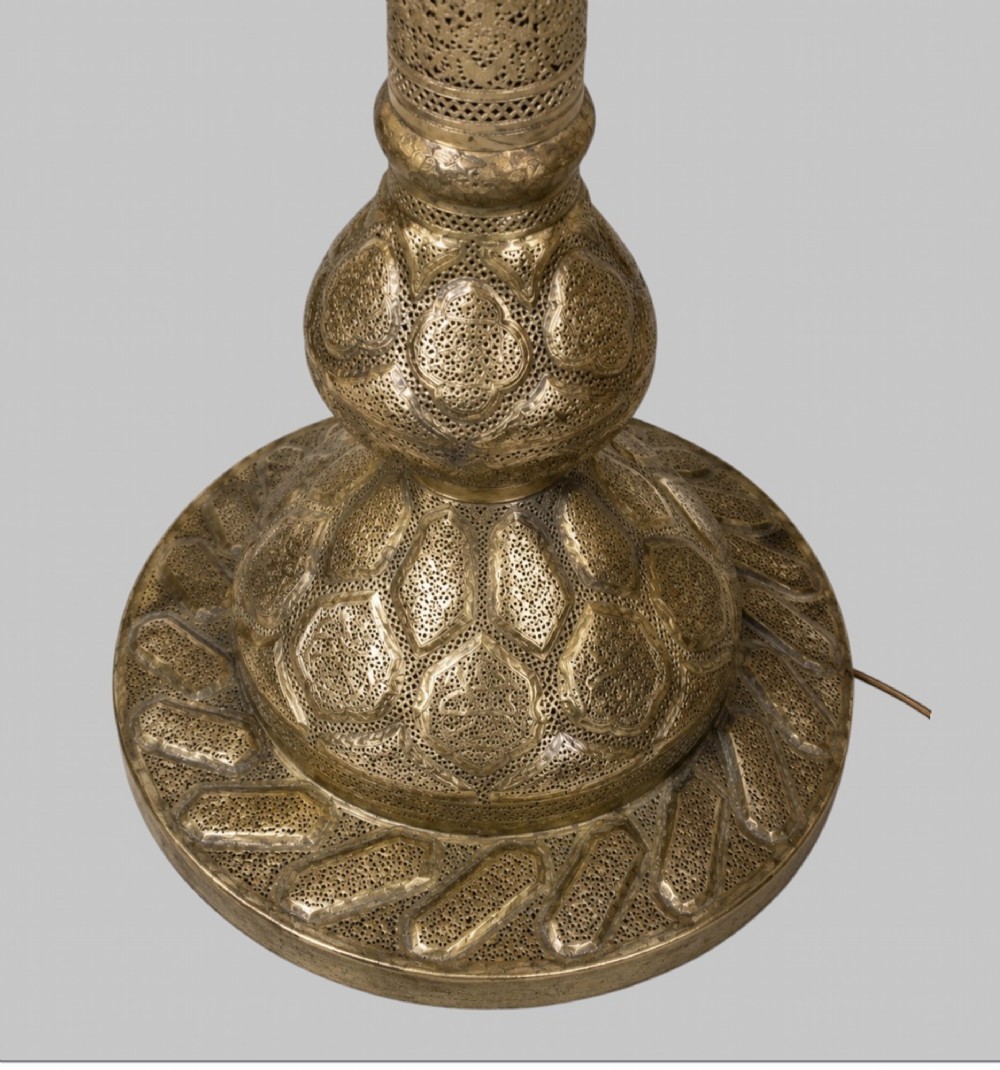 A tall Middle Eastern style brass floor lamp with an intricate pierced shade, decorative central column, and a wide flared base. View VI