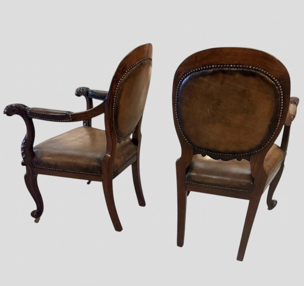A pair of carved rosewood armchairs featuring dark leather upholstery, brass stud detailing, carved elephant crests, lion-head armrests, and cabriole legs. View II