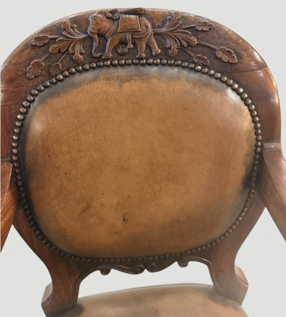 A pair of carved rosewood armchairs featuring dark leather upholstery, brass stud detailing, carved elephant crests, lion-head armrests, and cabriole legs. View IV