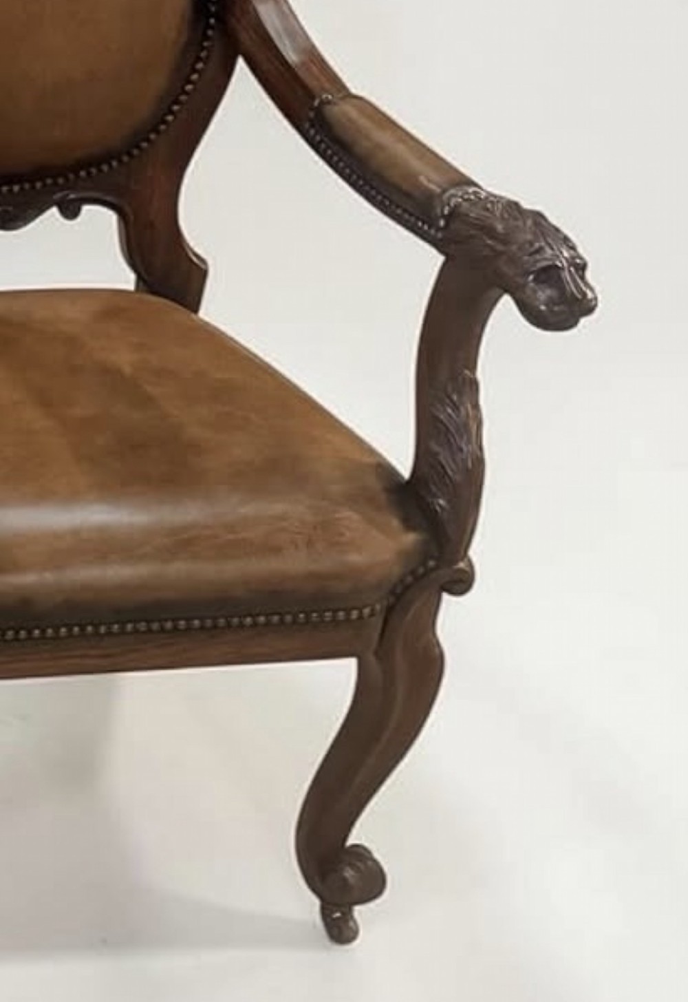 A pair of carved rosewood armchairs featuring dark leather upholstery, brass stud detailing, carved elephant crests, lion-head armrests, and cabriole legs. View VI