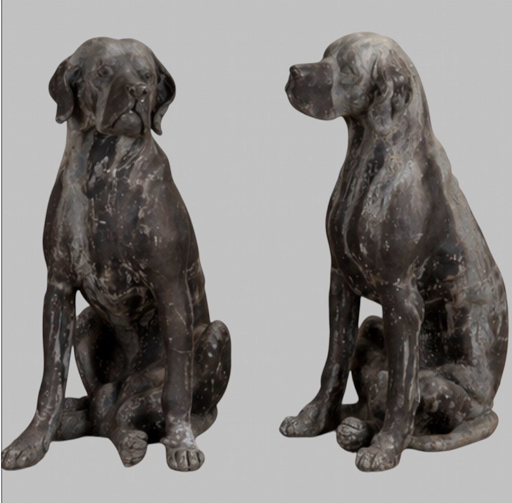 A pair of life-size cast lead sculptures depicting seated hounds with detailed anatomical features and a weathered grey surface.