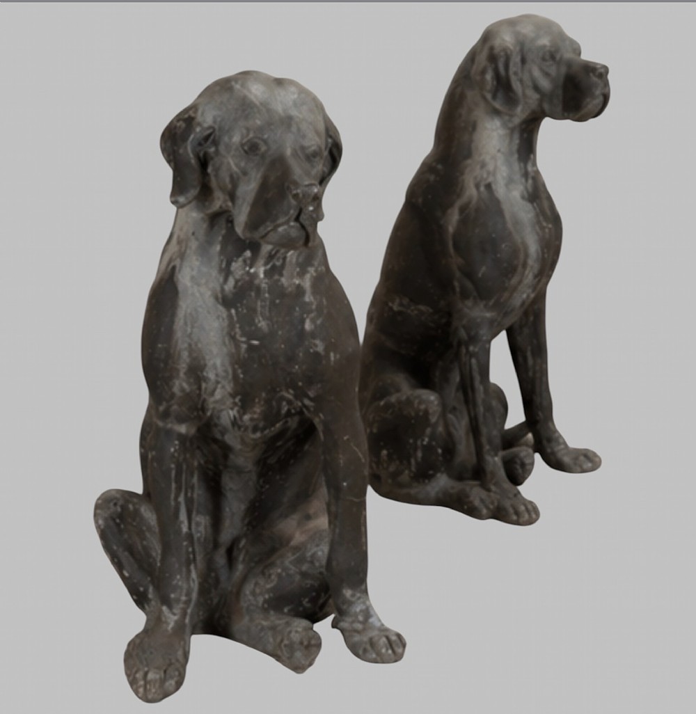 A pair of life-size cast lead sculptures depicting seated hounds with detailed anatomical features and a weathered grey surface. View II