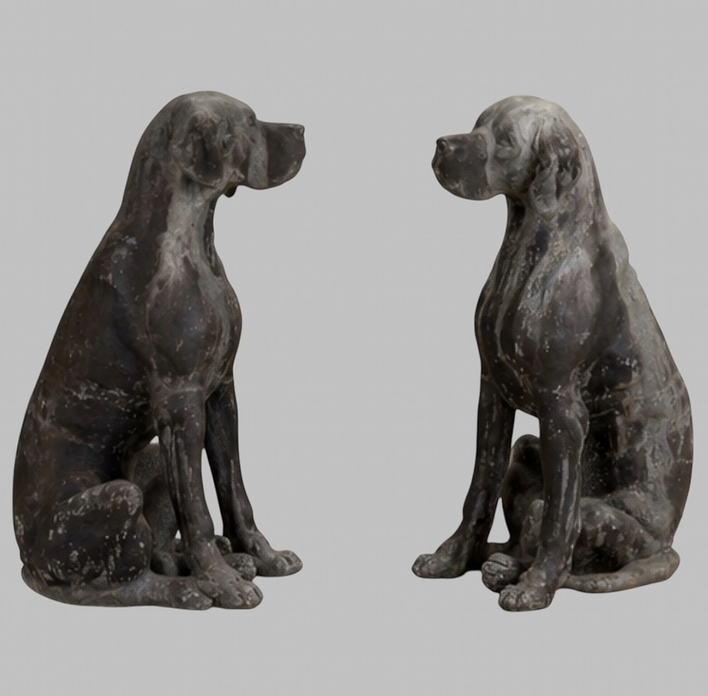 A pair of life-size cast lead sculptures depicting seated hounds with detailed anatomical features and a weathered grey surface. View V