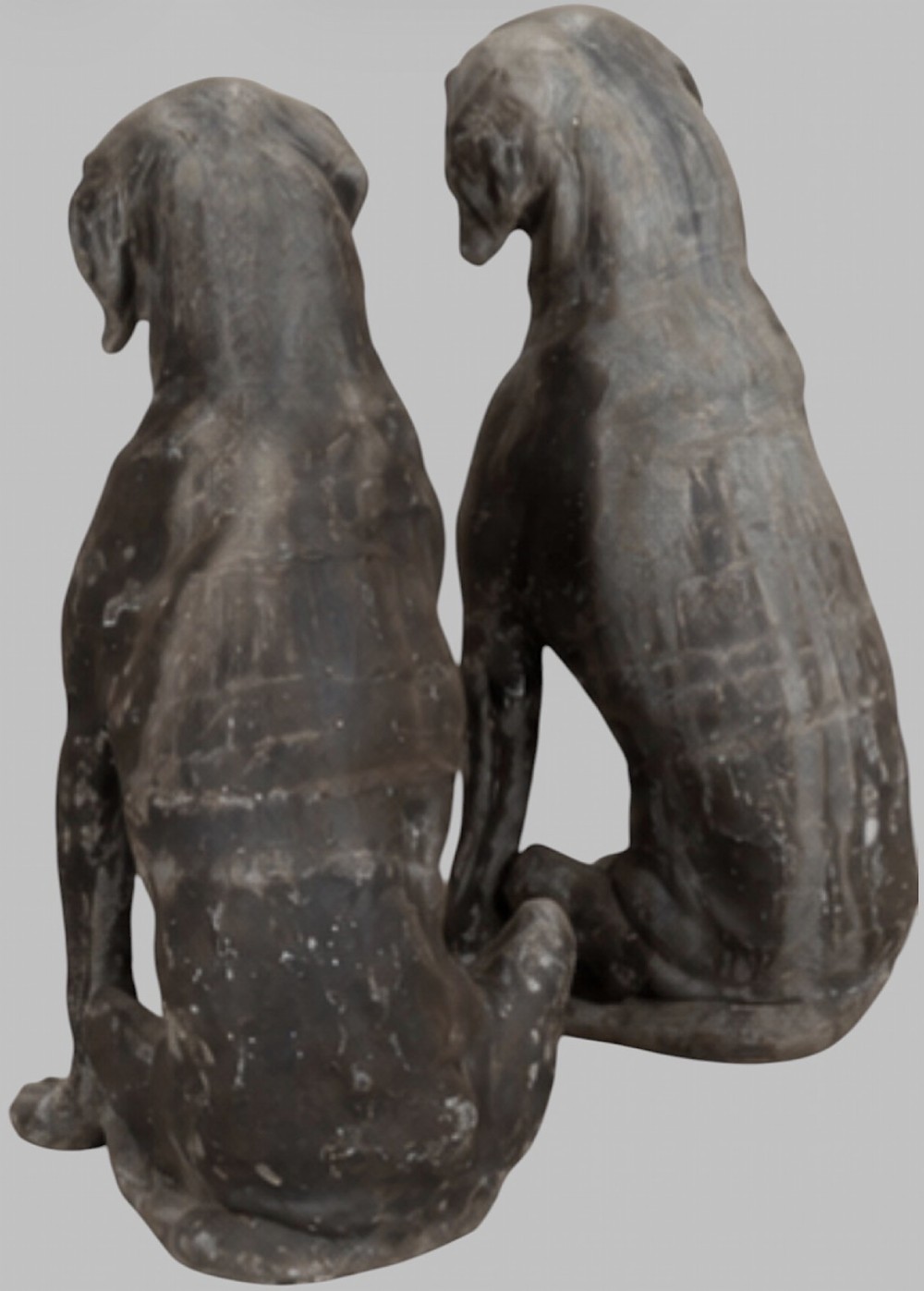 A pair of life-size cast lead sculptures depicting seated hounds with detailed anatomical features and a weathered grey surface. View VI