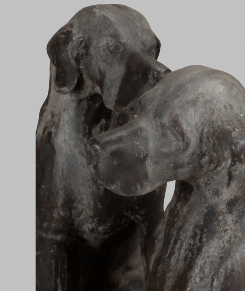 A pair of life-size cast lead sculptures depicting seated hounds with detailed anatomical features and a weathered grey surface. View VII