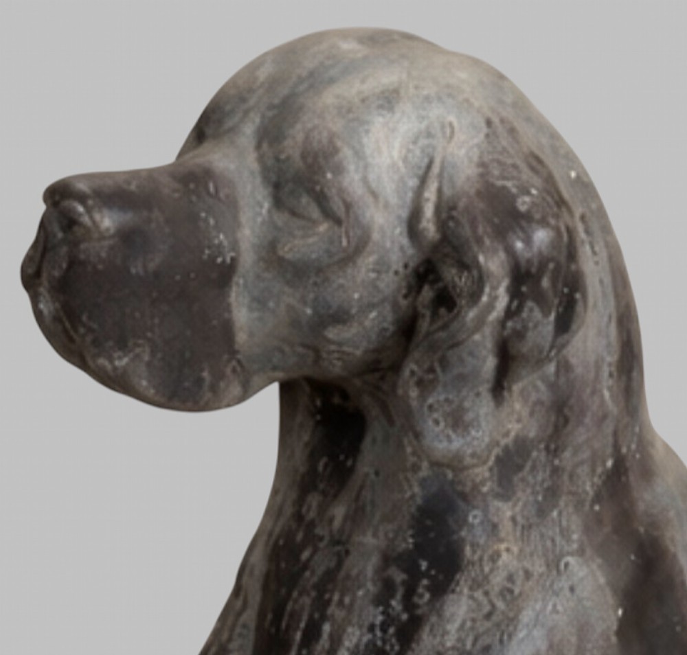 A pair of life-size cast lead sculptures depicting seated hounds with detailed anatomical features and a weathered grey surface. View IX