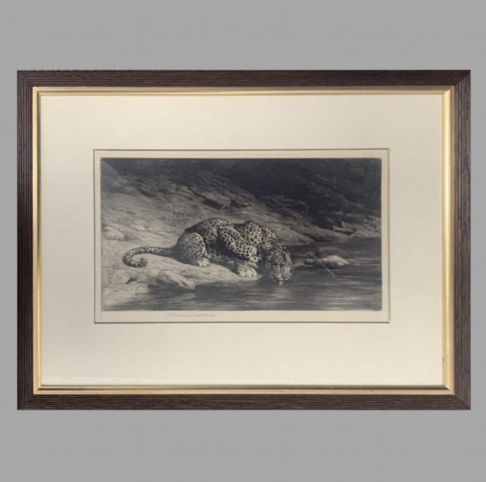 A framed monochrome etching depicting a crouching leopard drinking water from a stream against a rocky background.