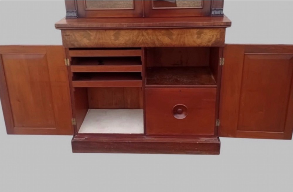 An early Victorian mahogany two-height library bookcase featuring upper glazed doors, flame mahogany lower panels, and carved pilasters. View IV