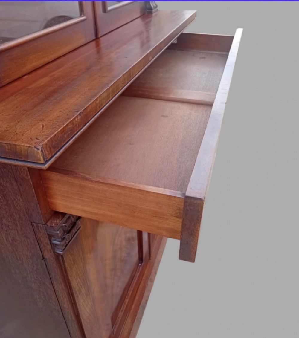An early Victorian mahogany two-height library bookcase featuring upper glazed doors, flame mahogany lower panels, and carved pilasters. View V