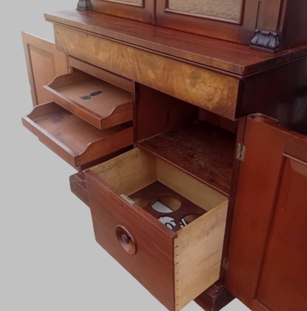 An early Victorian mahogany two-height library bookcase featuring upper glazed doors, flame mahogany lower panels, and carved pilasters. View VI