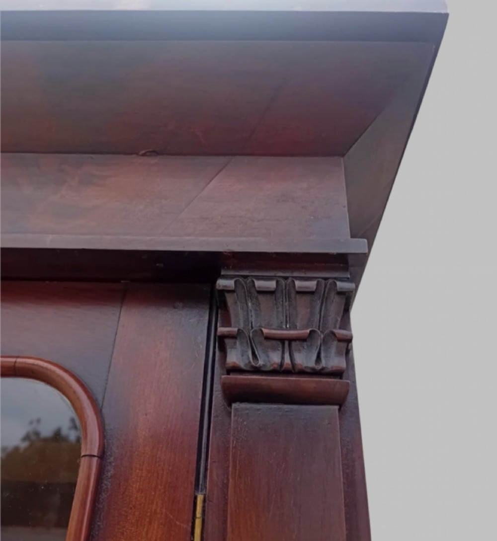An early Victorian mahogany two-height library bookcase featuring upper glazed doors, flame mahogany lower panels, and carved pilasters. View VII