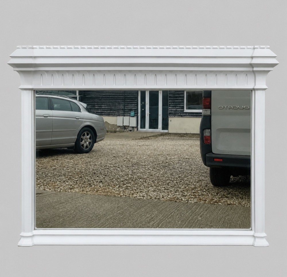 A large late Victorian rectangular overmantel mirror featuring a white painted wooden frame with a prominent corniced top and carved moulding.