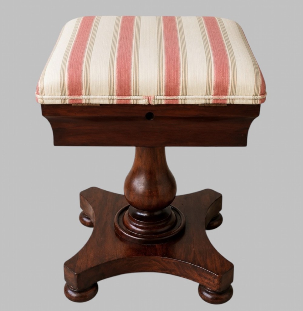 An upholstered William IV mahogany sewing box stool with red and cream striped fabric, mounted on a turned central pedestal and a concave platform base with bun feet.
