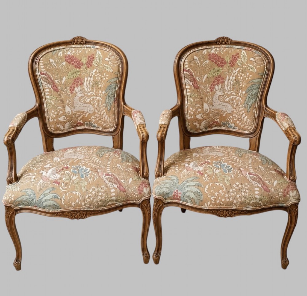 A pair of Neo-Rococo open armchairs featuring carved wooden frames, cabriole legs, and botanical tapestry upholstery.