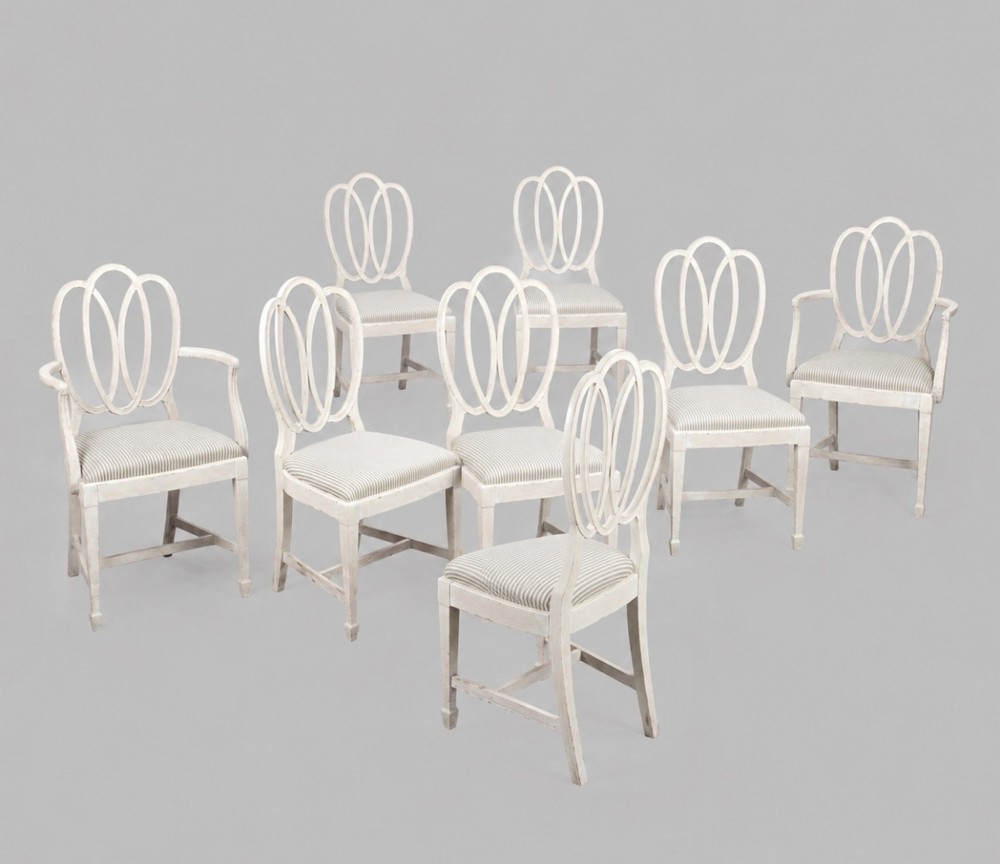 A set of eight off-white painted dining chairs featuring interlocking oval backrests, striped upholstered seats, including two carver armchairs and six side chairs.