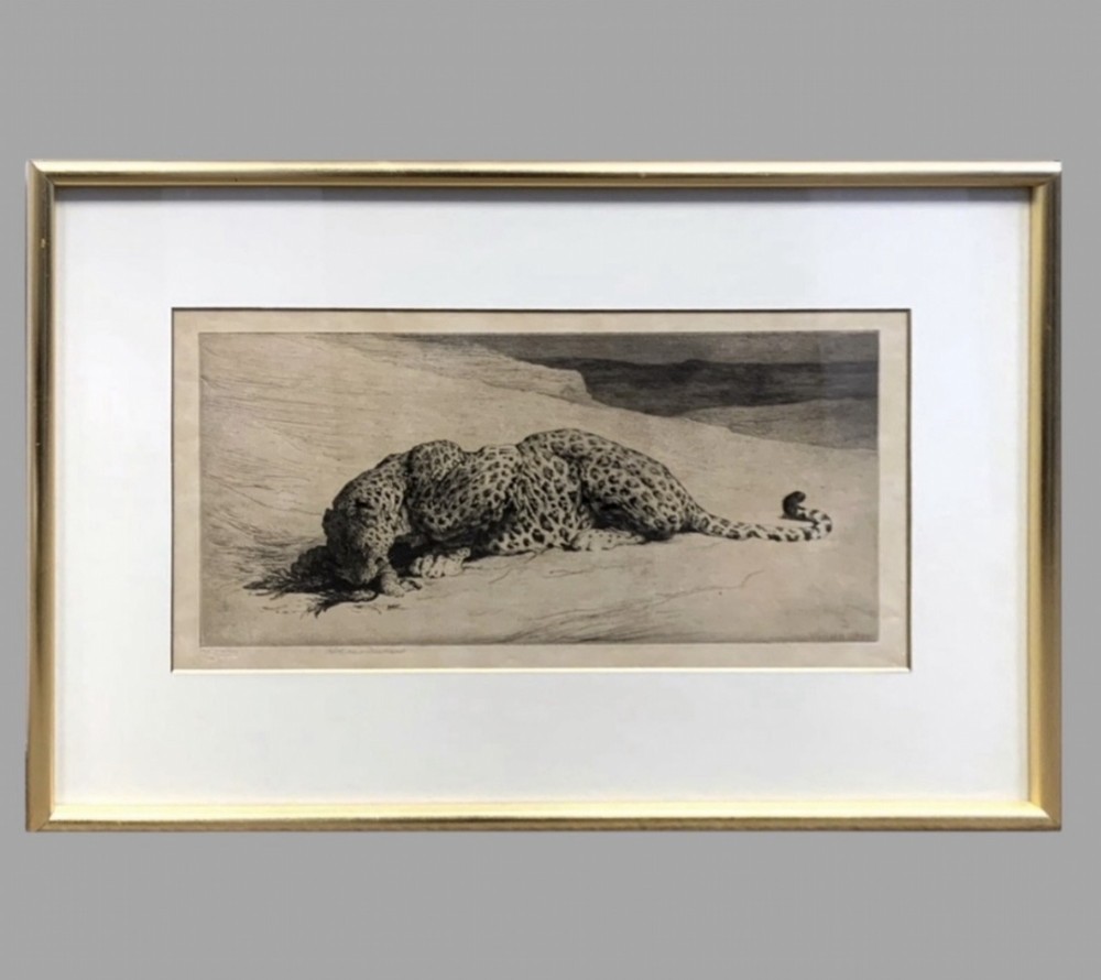 A horizontal monochrome etching depicting a leopard crouching on sandy ground, presented in a cream mount and slim gilt frame.