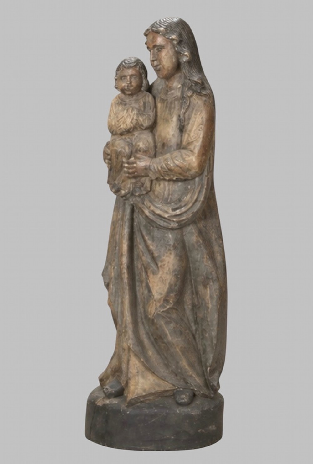 A carved wooden statue depicting the Virgin Mary holding the Infant Jesus on an integrated round base.
