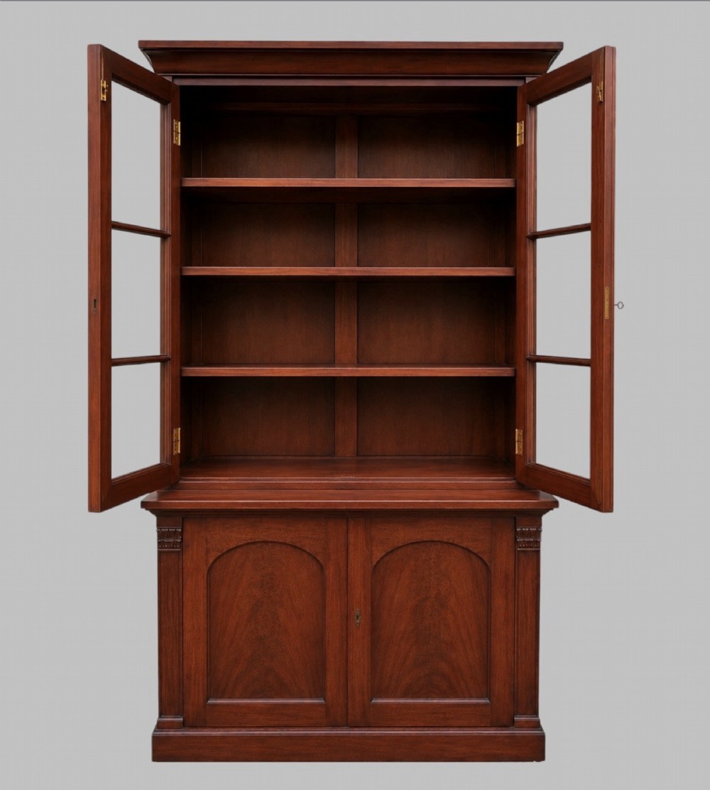 An early Victorian mahogany two-height library bookcase featuring upper glazed doors, flame mahogany lower panels, and carved pilasters. View VIII