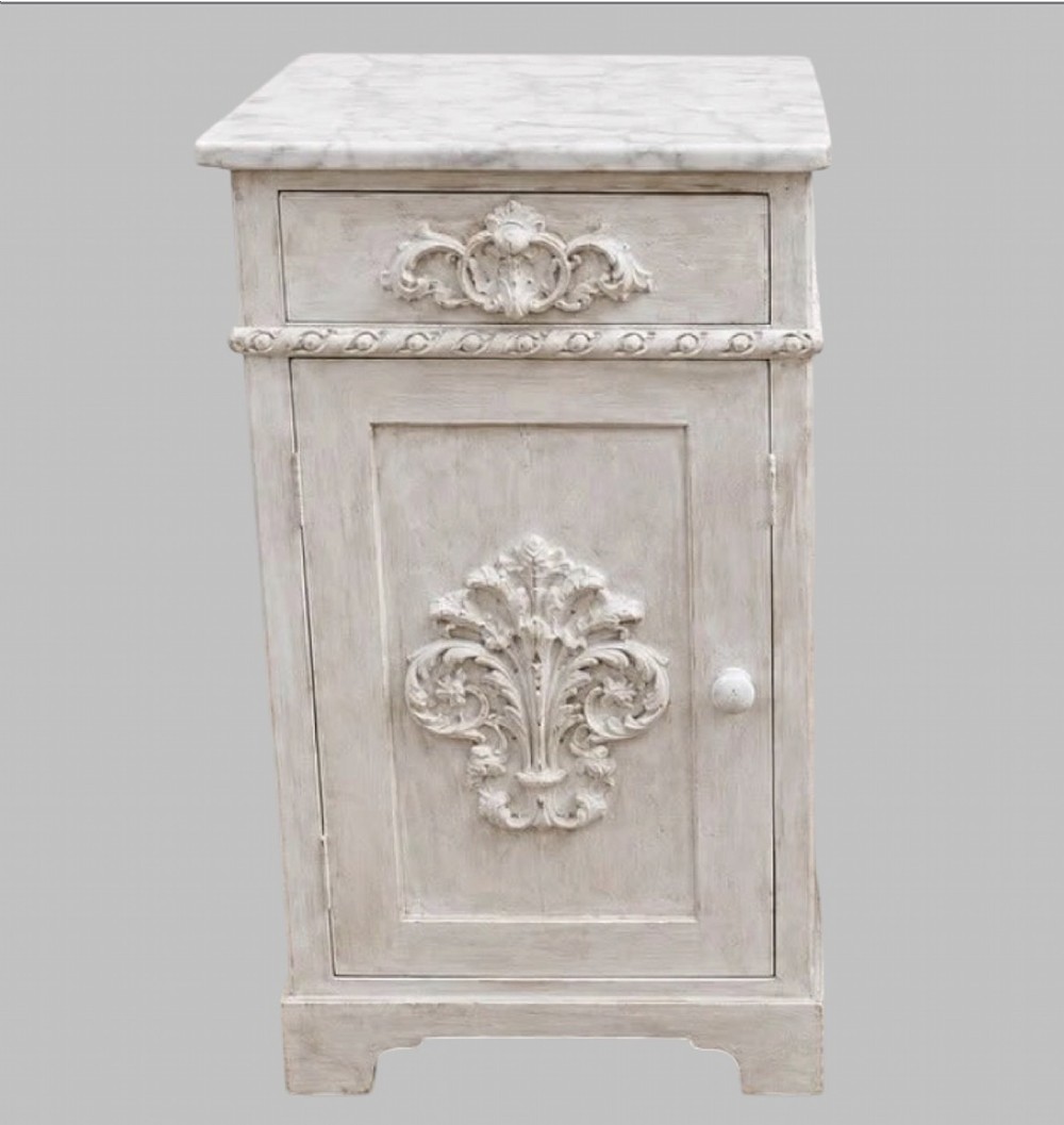 A pair of French off-white painted bedside cabinets featuring fitted marble tops, single drawers, and cupboard doors with central carved foliate relief motifs. View II
