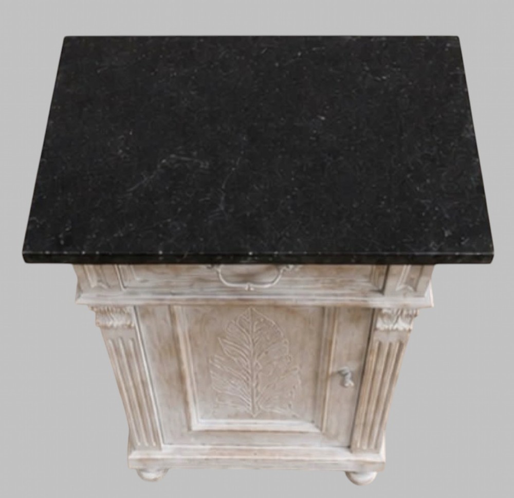 A pair of off-white painted wooden bedside cabinets with dark marble tops, single drawers, fluted pilasters, and carved leaf panels on the doors. View II