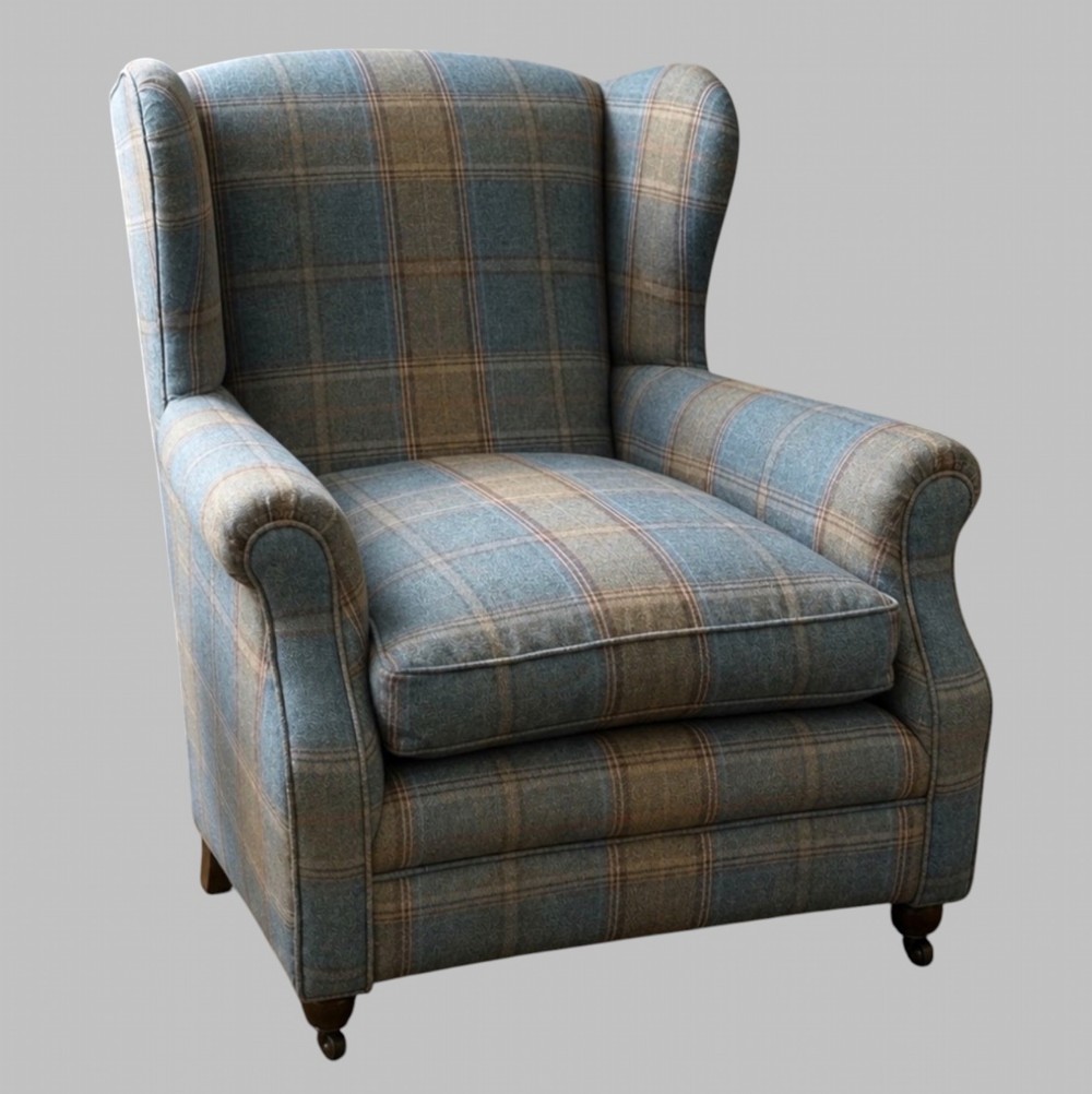A traditional English wingback armchair upholstered in a teal and tan plaid Shetland wool pattern with turned front legs on brass castors.