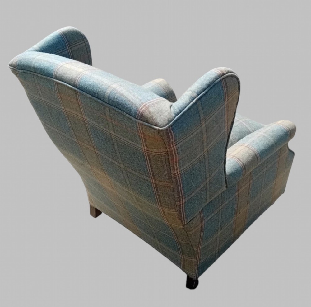 A traditional English wingback armchair upholstered in a teal and tan plaid Shetland wool pattern with turned front legs on brass castors. View V