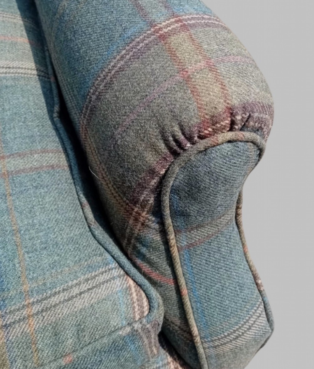 A traditional English wingback armchair upholstered in a teal and tan plaid Shetland wool pattern with turned front legs on brass castors. View VI