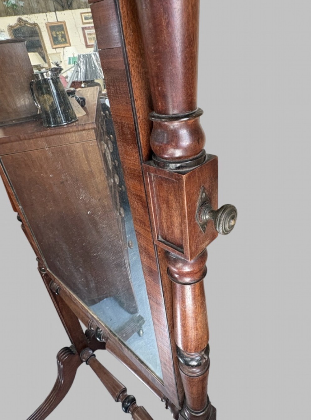 A nineteenth-century flame mahogany cheval mirror featuring turned side uprights, top finials, reeded splayed legs, and brass castors. View IV