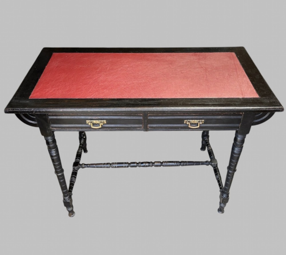 A late Victorian ebonised writing desk featuring a red leather top insert, two drawers with brass handles, turned legs, and an H-stretcher. View II
